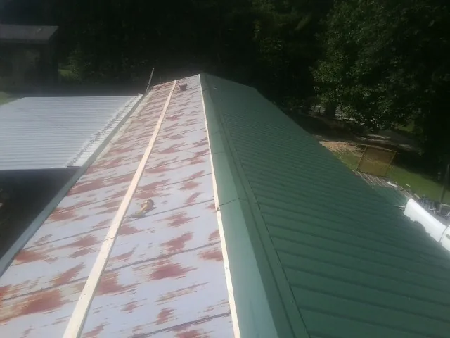 Old rusted panels beside newly installed green metal roofing — Wind Damage Roof Repair by Roofing Brothers in Claryville