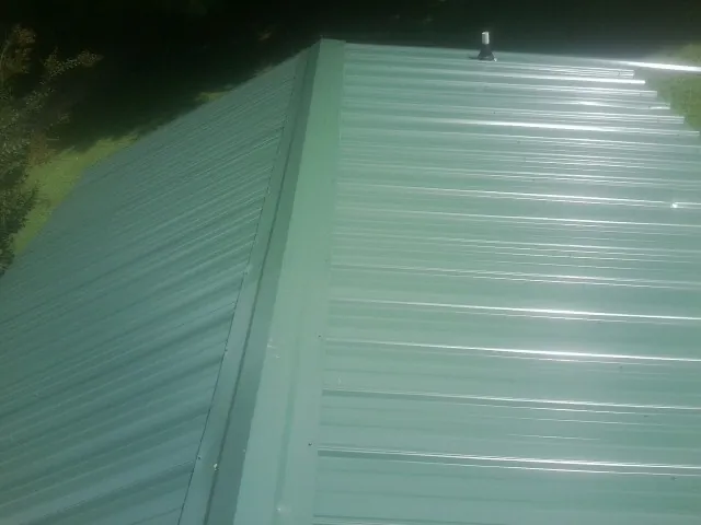 New green metal panels meeting at the ridge of a roof — Flat Roof Repair work by our crew in Claryville