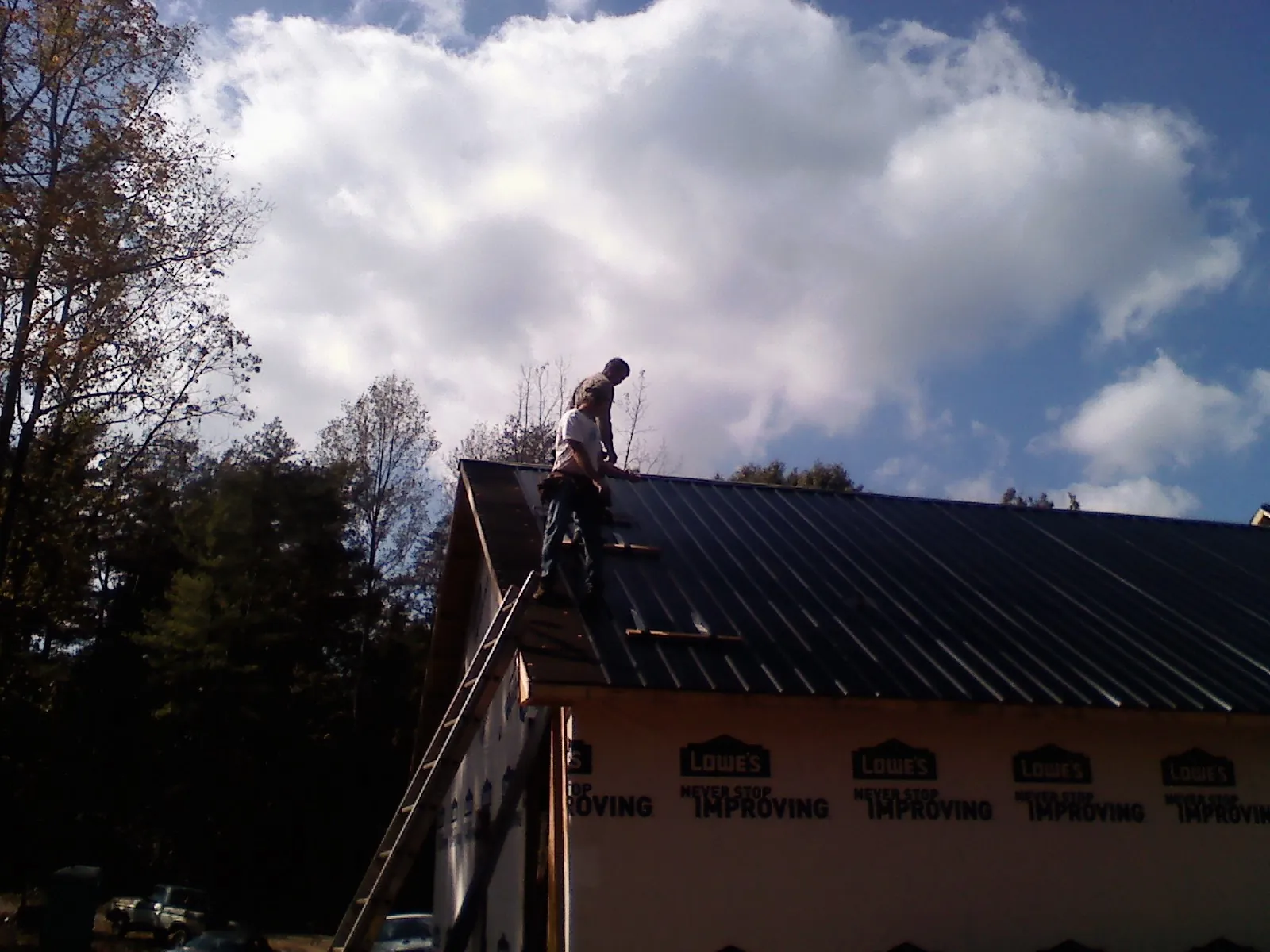 Roofer fastening dark metal panels high against a cloudy sky, from a Roof Inspection job in Claryville