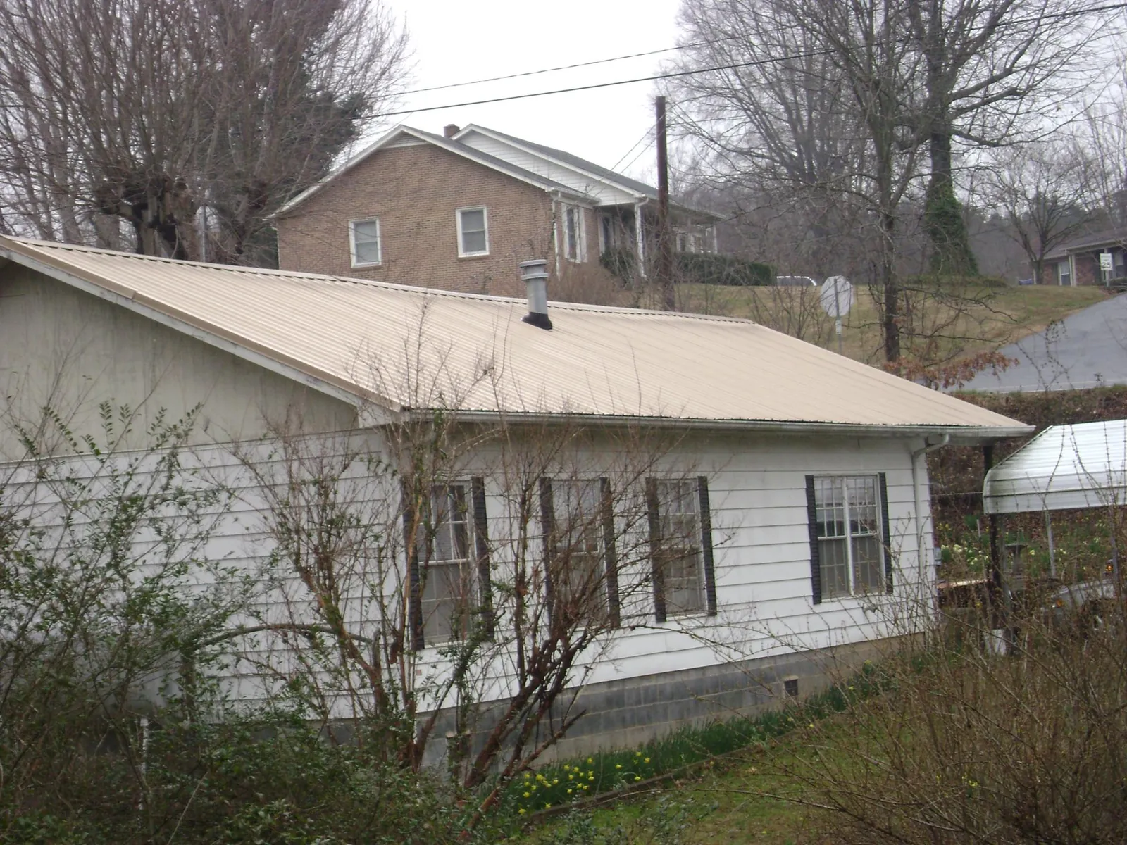 Tan metal roof on a white sided house set into a hillside — Commercial Roofing by Roofing Brothers in Claryville