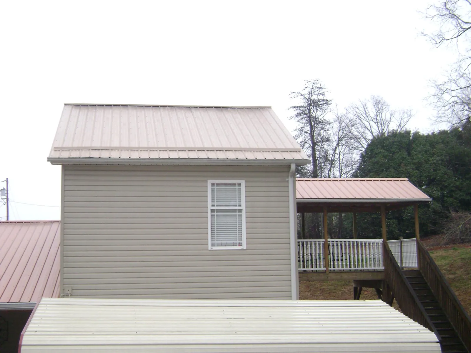 Tan metal roofs on a two story addition and attached porch, from a Roof Replacement job in Claryville